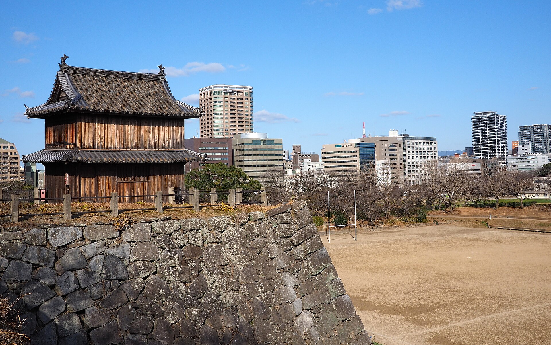 福岡城跡の石垣の上に建つ木造の櫓と、その向こうの福岡市街