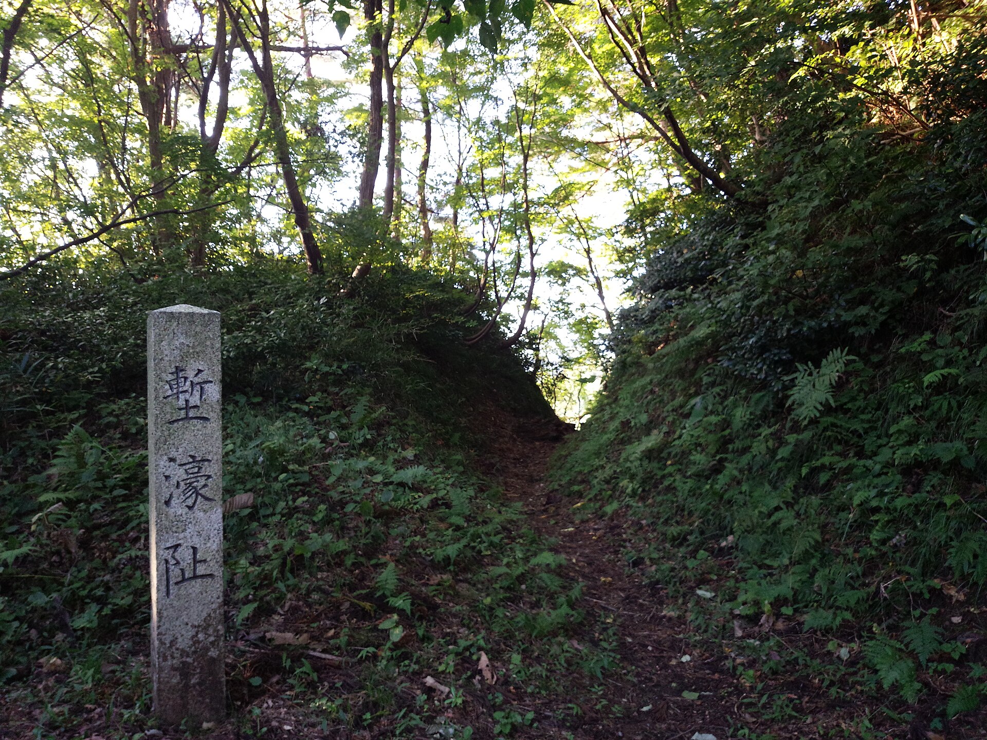 春日山城跡の堀切の跡。「塹濠址」と刻まれた石柱の先に、木立の中の山道が続く