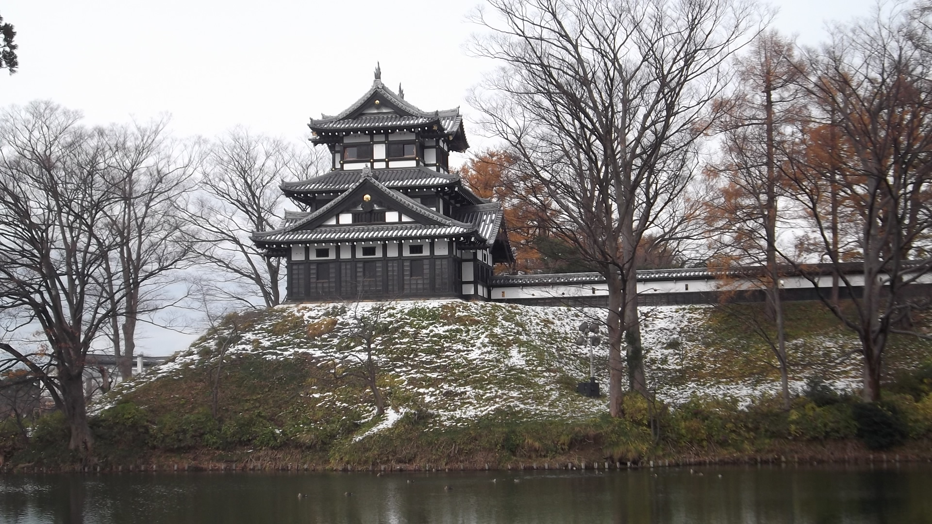 高田城三重櫓を堀の向こうから望む。うっすら雪の残る土塁と、色づいた木々。12月初めの撮影