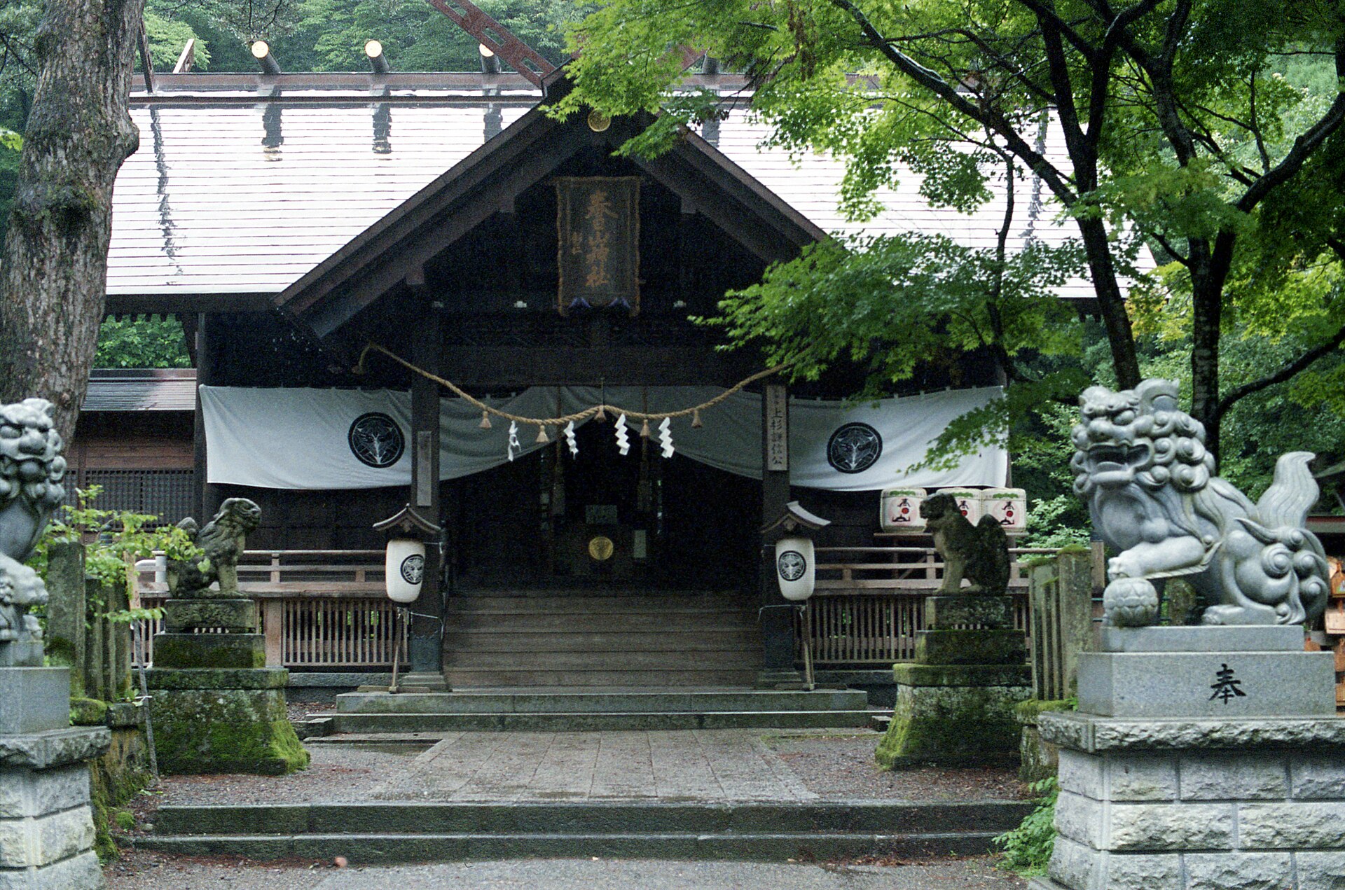 春日山神社の拝殿を正面から。左右に狛犬が並び、紋の入った白い幕が張られている