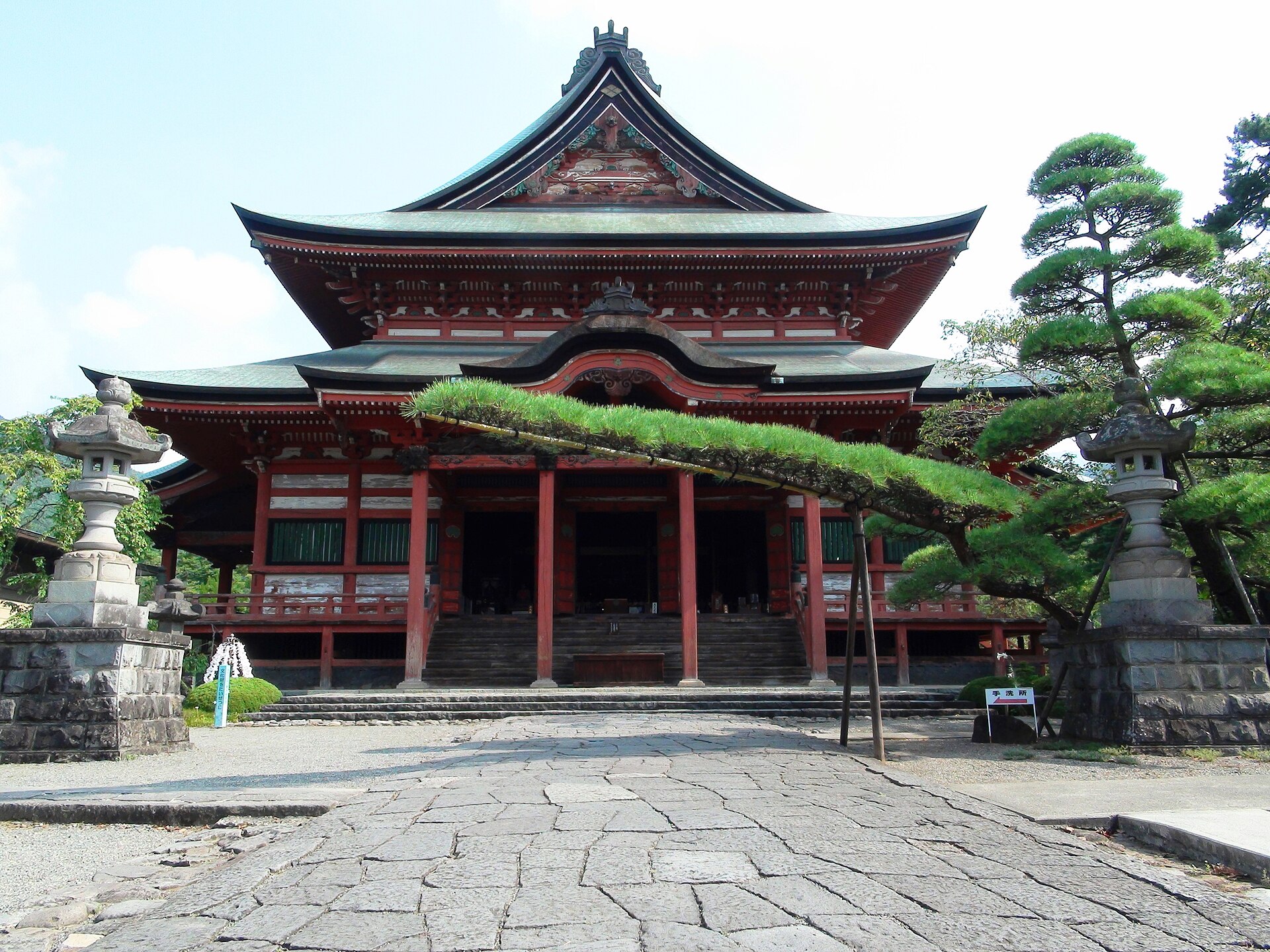 甲斐善光寺の金堂を、正面の石畳から。重なる屋根の形と、両脇の石灯籠にも目を向けて