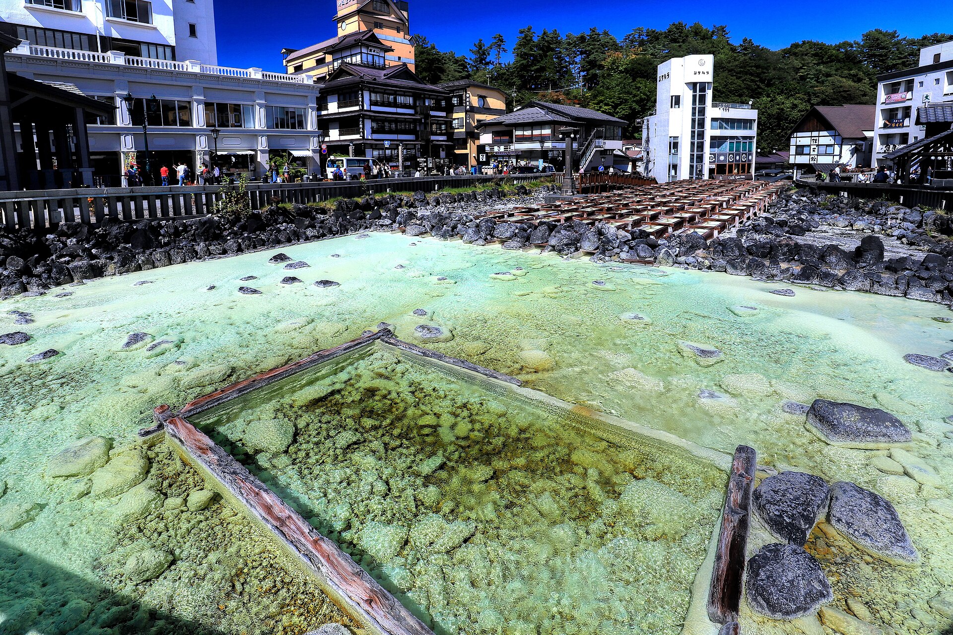 湯畑。奥に木の樋が並び、手前に青白い湯がたまっています