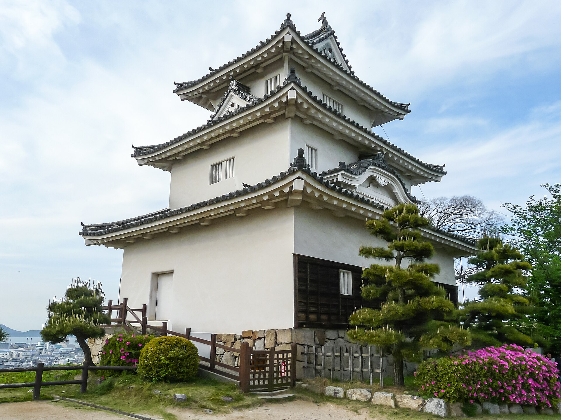 丸亀城の天守を本丸から見た南西面。石垣の上に建つ三層の天守と手前の松