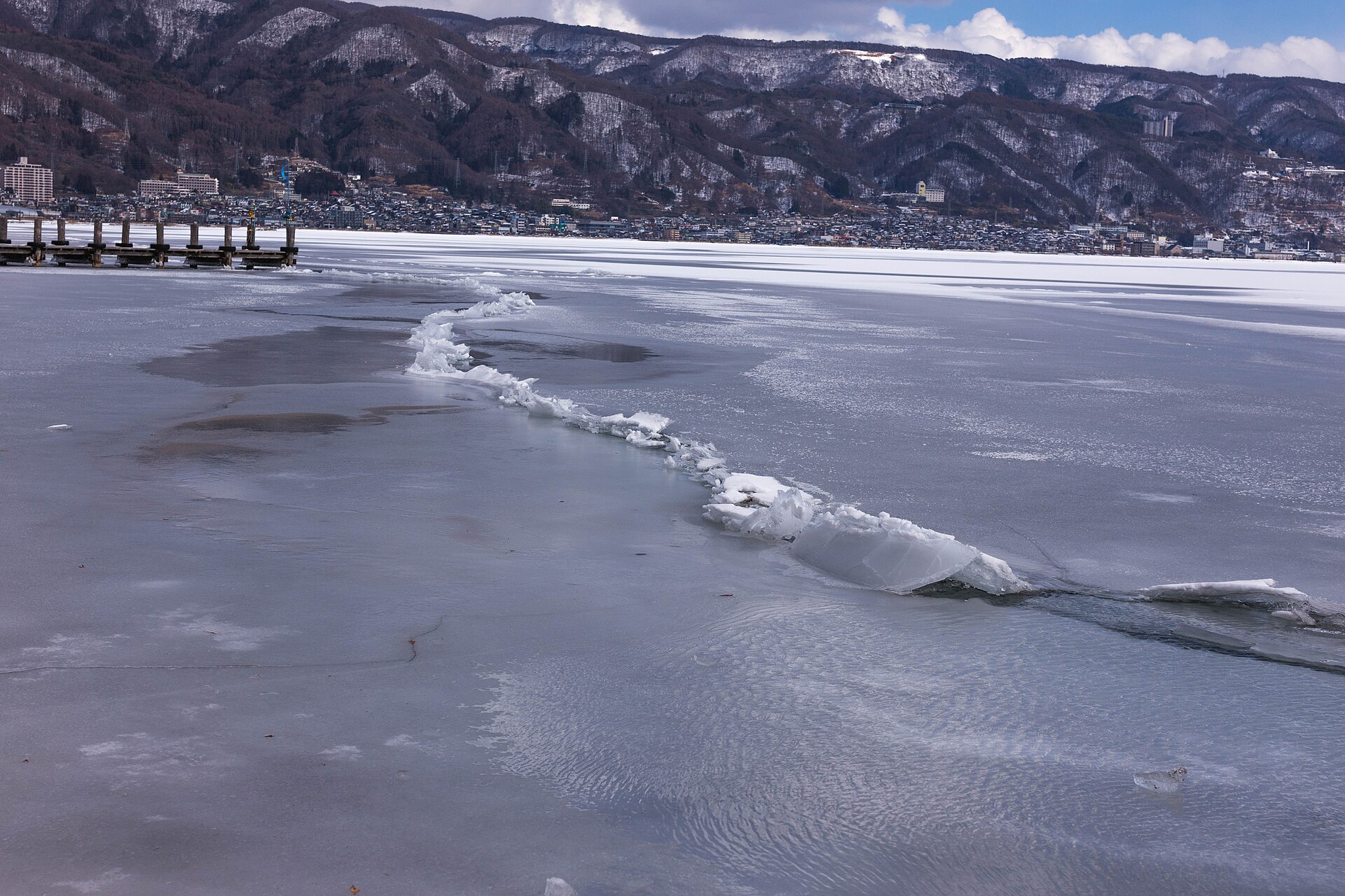 全面に凍った諏訪湖。せり上がった氷が筋になって、手前から対岸の市街へ向かって伸びる
